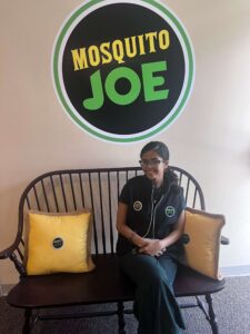 Mosquito Joe of South Central PA team member, Mary sitting on bench under a Mosquito Joe sign. 